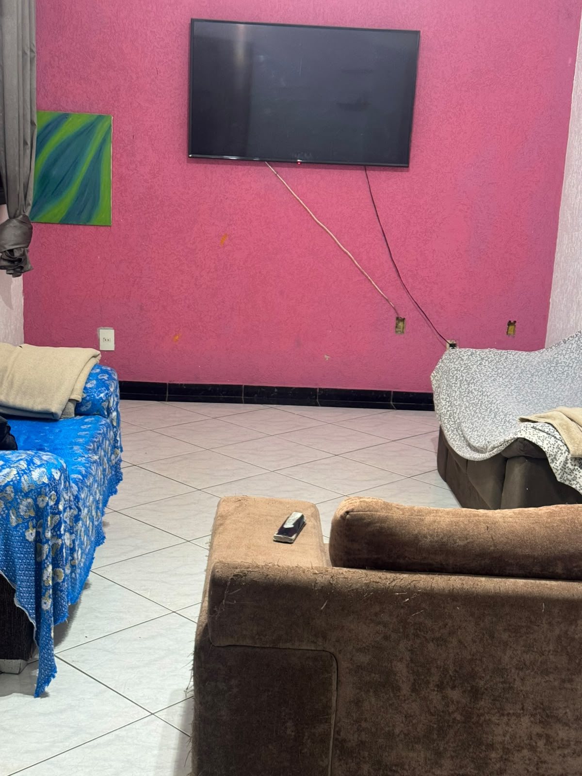um quarto de estar com TV na parede rosa, sofá azul e outro em couro, tapete e pintura na parede  — texto: