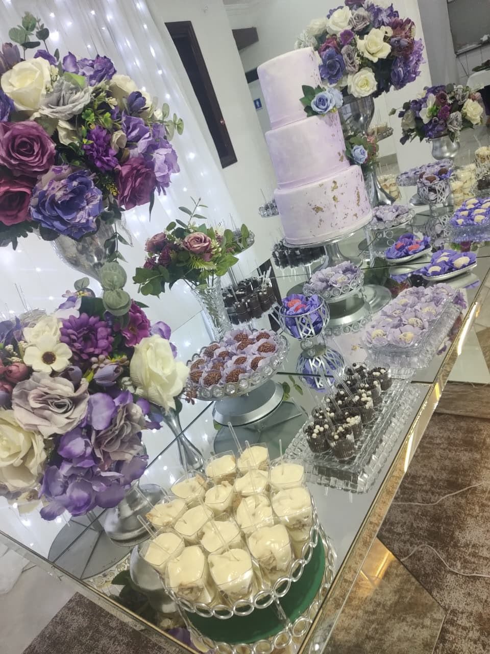 mesa de doces e flores para festa de casamento, com cake pop, bolo de casamento e arranjos de flores em tons de roxo e branco