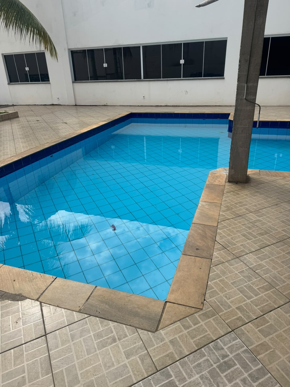 Piscina azulejada azul da Chácara Oliver, com borda de pedra e prédio branco ao fundo